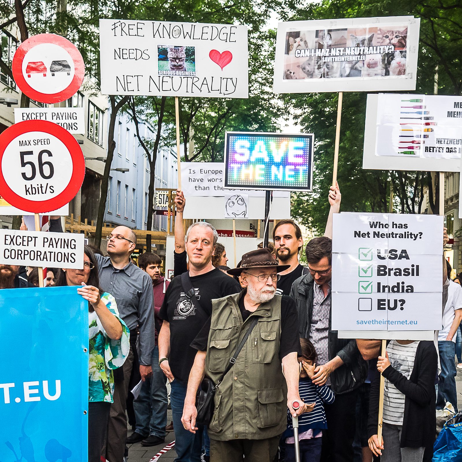 Crowd at the 2016 Vienna save-the-internet protest holding signs including &ldquo;Free knowledge needs net neutrality&rdquo; and a &ldquo;56 kbit/s&rdquo; speed-limit sign
